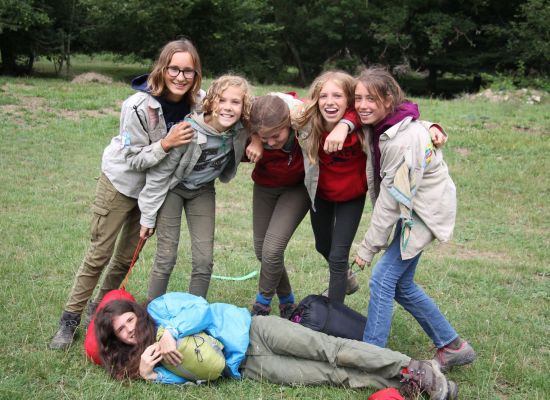 zes jonggidsen poseren met hun slaapzak, eentje ligt plat op de grond