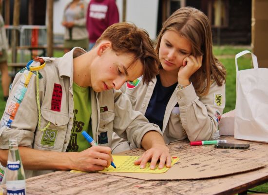 scout en gids overleggen. De scout noteert iets.