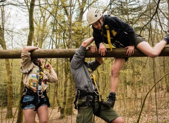 Begeleider helpt scout op het touwenparcour