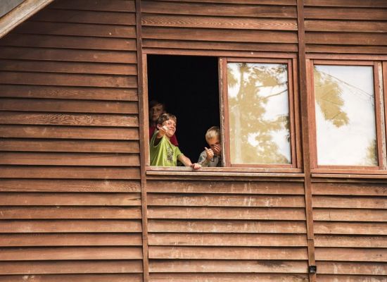 Drie scoutsleden kijken door het raam van een blokhut