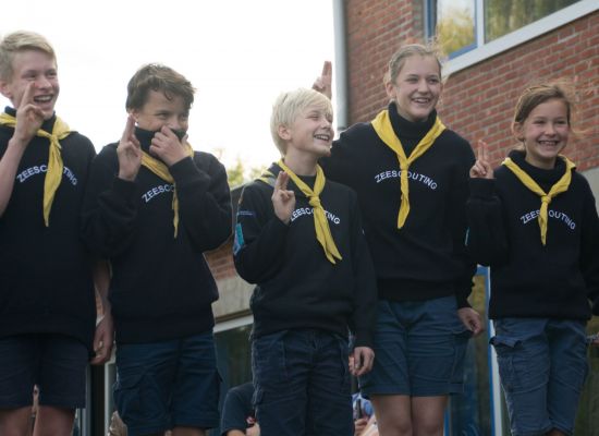 Vijf zeescouts, in patrouille, doen de scoutsgroet