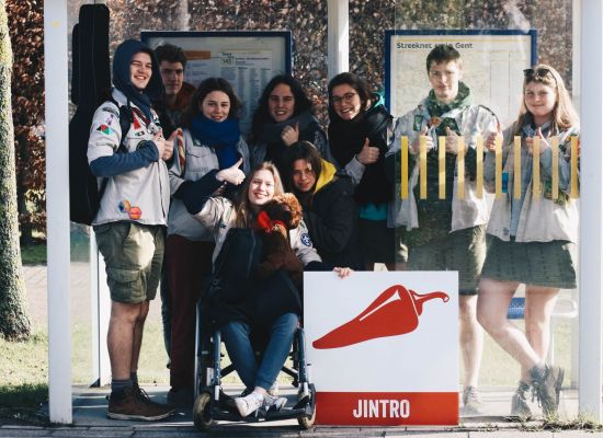 Een groep leiding, eentje in een rolstoel, vult een bushok en poseert, duim omhoog, met het Jintrobord.