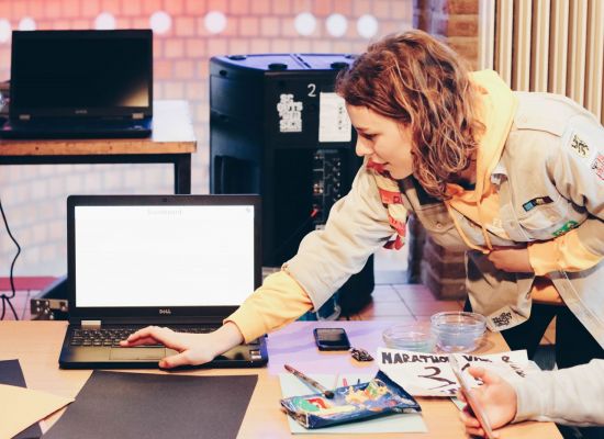 een leidster staat over een laptop gebogen en klikt wat aan