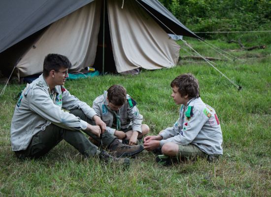 Een leider en twee leden praten al zittend voor hun tent.