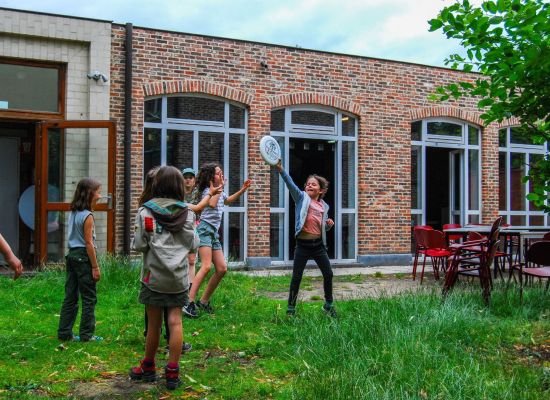 Leden spelen in het gras voor hun scoutslokaal