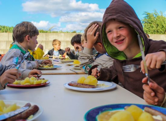 Welpen zitten aan gesjorder tafel te eten op kamp
