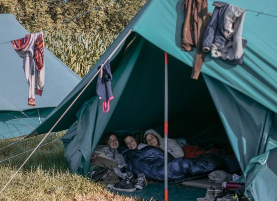 tent met 3 scoutsmeisjes, boven de tent hangen kleren te drogen