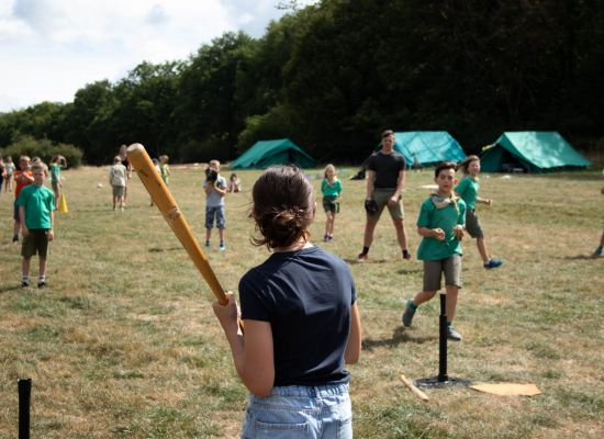 Een meisje staat klaar met een baseballbat, in het veld staan andere spelers klaar. 