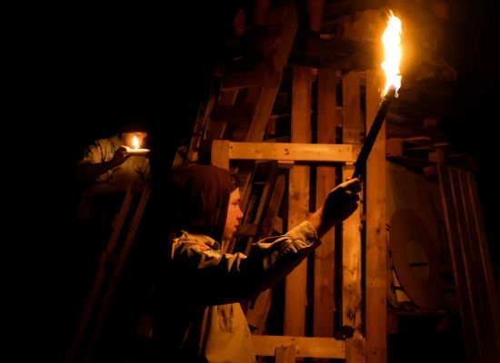 een jonggiver in het donker met een fakkel bij een houtstapel