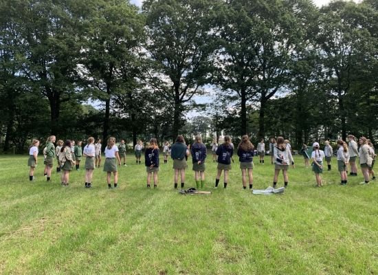 Scoutsgroep staat in een grote kring op een grasveld