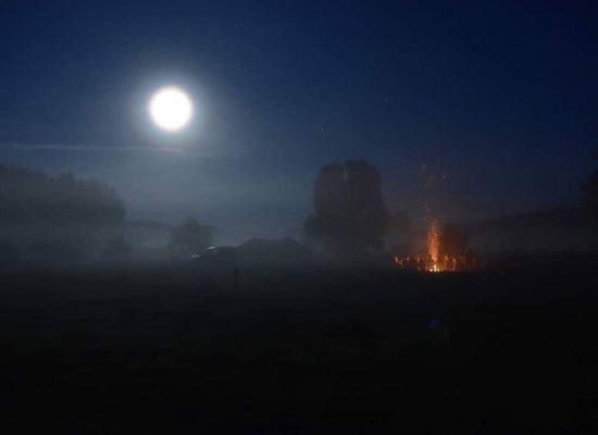 Brandend kampvuur op kampterrein dat baadt in het maanlicht.