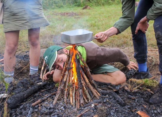 3 scouts rond houtvuur, ze blazen om vuur aan te wakkeren