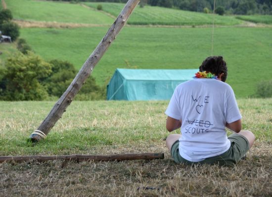 Giver die in het gras zit met een tshirt waar op staat dat hij niet van 'weed' maar van de scouts houdt. 