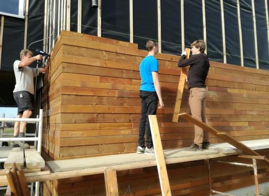 3 mannen timmeren planken tegen een lokaal