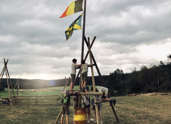 twee jongens staan op een driepikkel en plaatsen er een vlaggenmast op