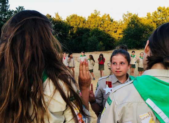 kabouters in formatie. Op de voorgrond groeten een leidster en een kabouter elkaar met de scoutsgroet.