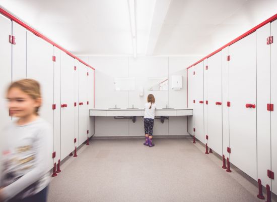 een meisje wast haar handen in een wc, een ander meisje loopt wazig uit beeld.