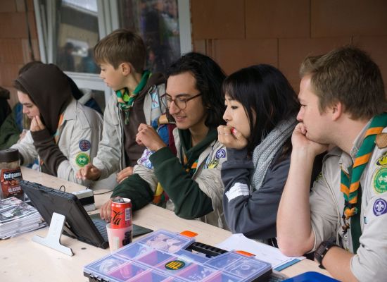Leden en leiding zitten aan een tafel waar je je kan inschrijven voor een scoutsevenement