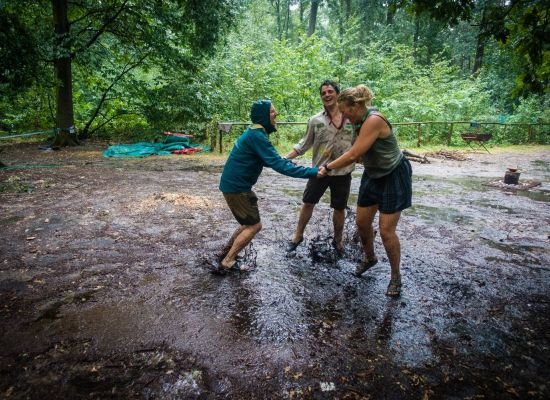 Twee meisjes en een jongen dansen in de regen met hun voeten in de modder.