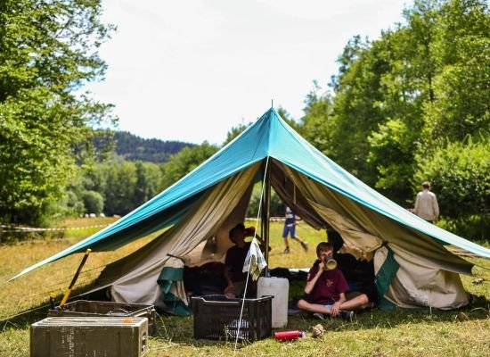 Een open staande patrouilletent. in de tent twee jongverkenners aan het uitrusten.