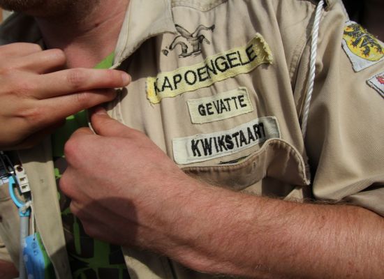 een leider met totem kapoengele gevatte kwikstaart knoopt zijn scoutshemd toe