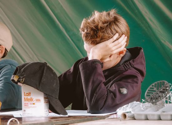 Jongen zit aan tafel op kamp met hand tegen het hoofd