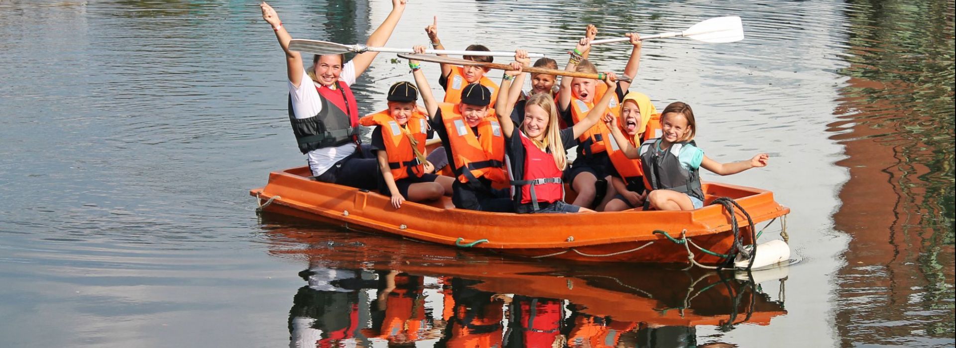 Kinderen met begeleider die met reddingsvesten in een raft zitten.