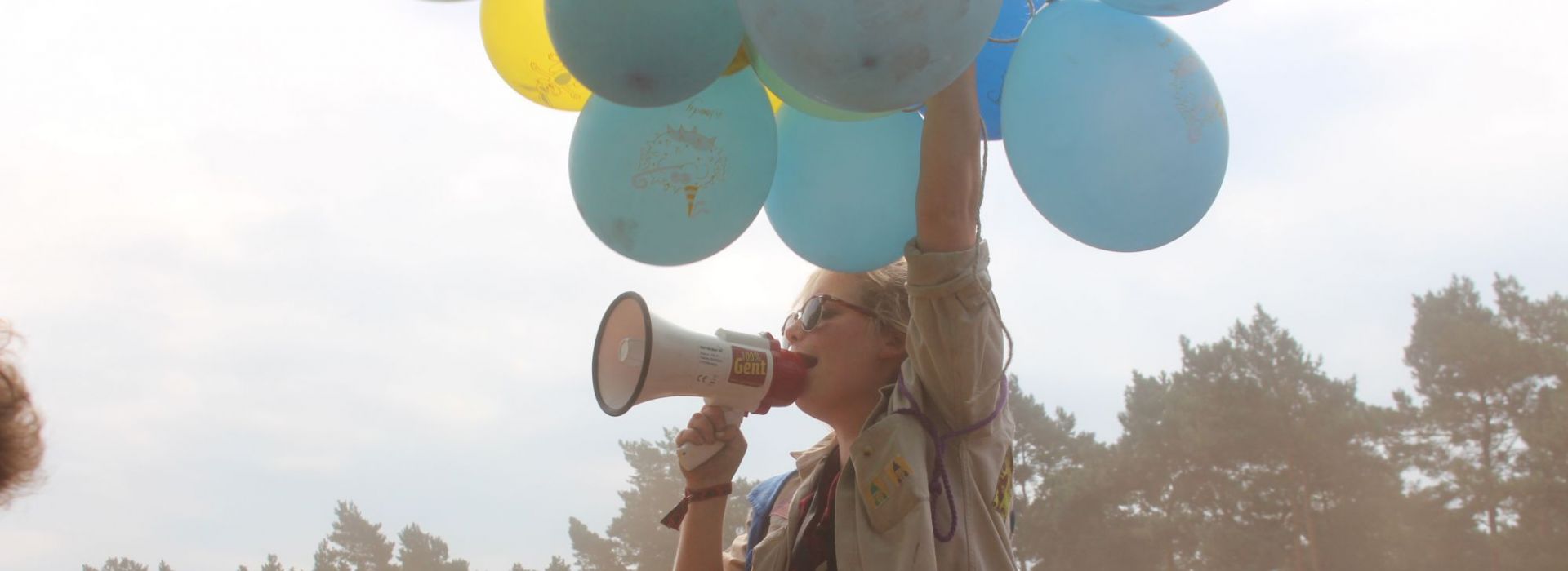 Meisje met megafoon en tros ballonnen zit op schouders van jongen.